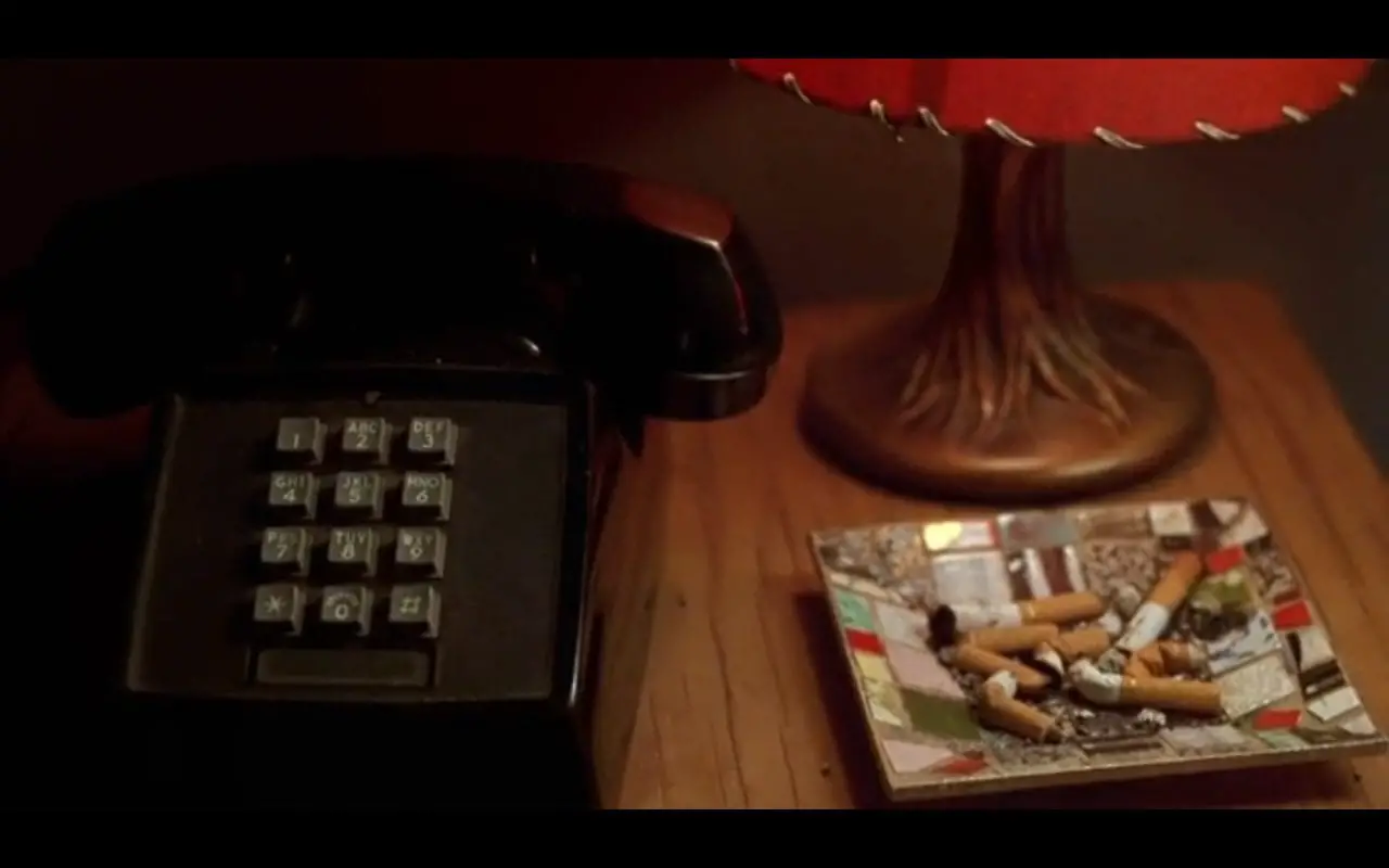 A closeup shoy of a bedstand on which there is a telephone, a lamp, and an ashtray full of butts from American Spirit cigarettes in David Lynch's Mulholland Drive