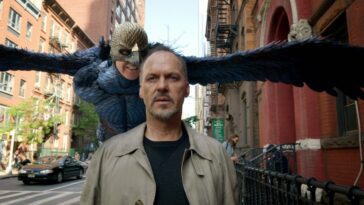 Birdman flies behind Michael Keaton on the street