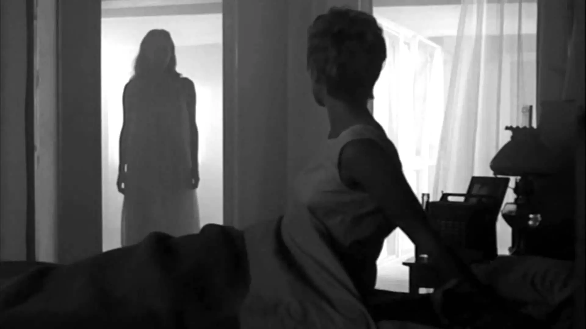 a woman sits upright in bed and sees a female figure looming in her bedroom doorway