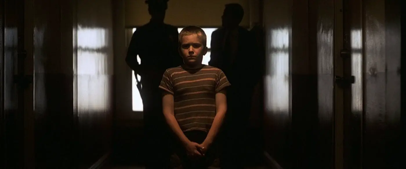 a young boy in a striped shirt stands in a hallway with two cops behind him looking upset
