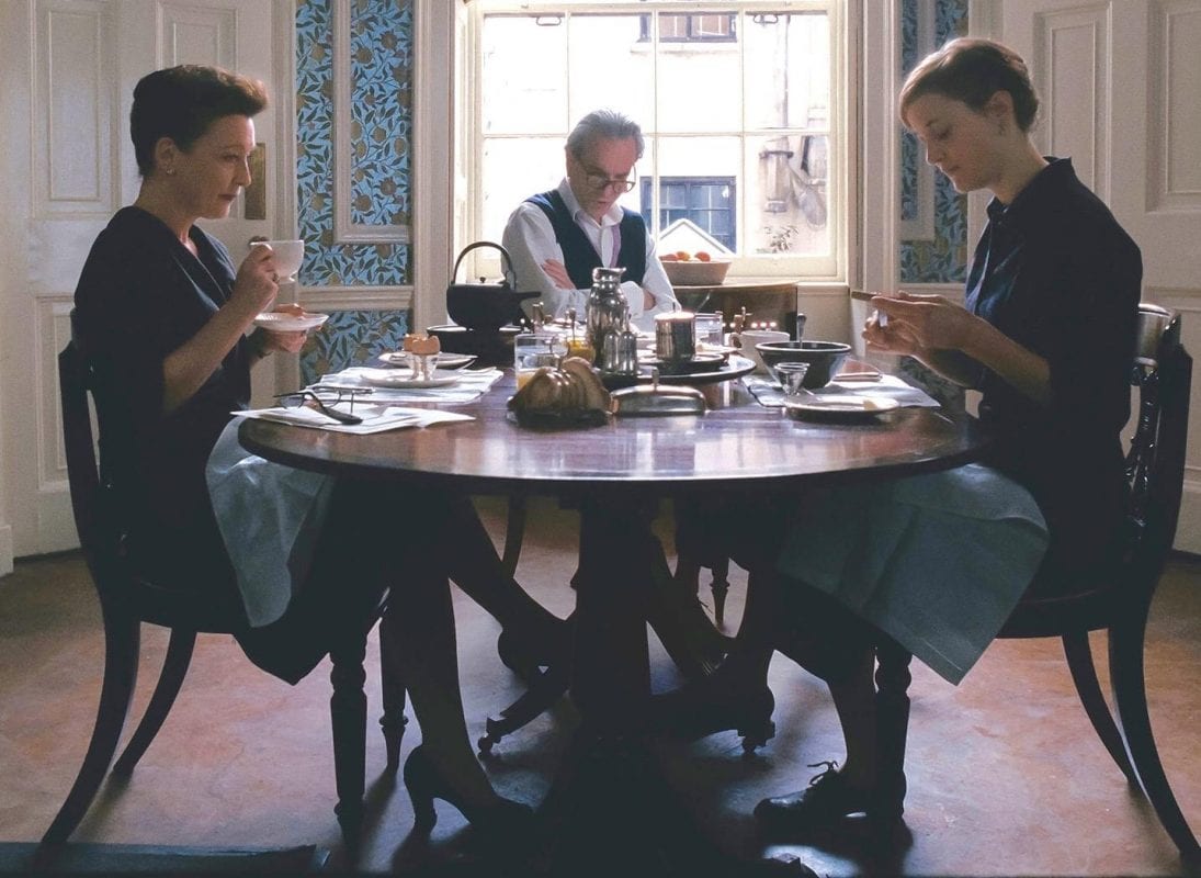 a woman and her parents sit at a dining table drinking tea very formally