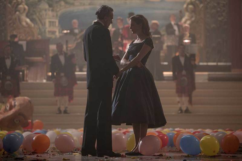 a male and female at the end of a party, balloons scattered at their feet and a band wearing kilts behind them