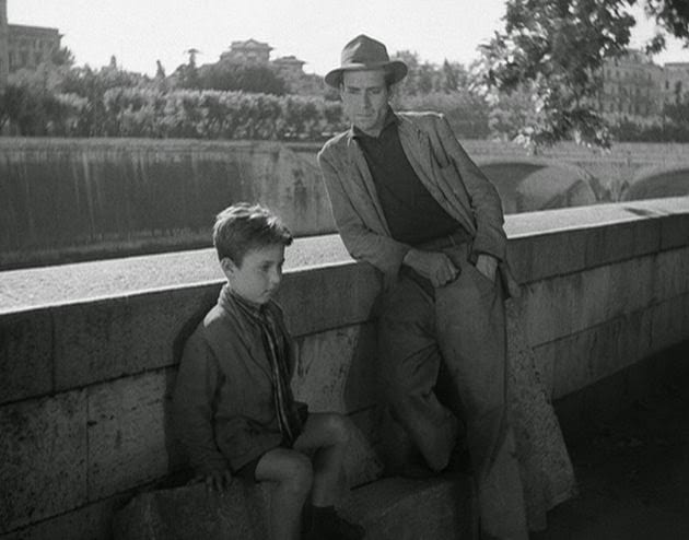 a boy sits and a mean leans against a bridge over a river
