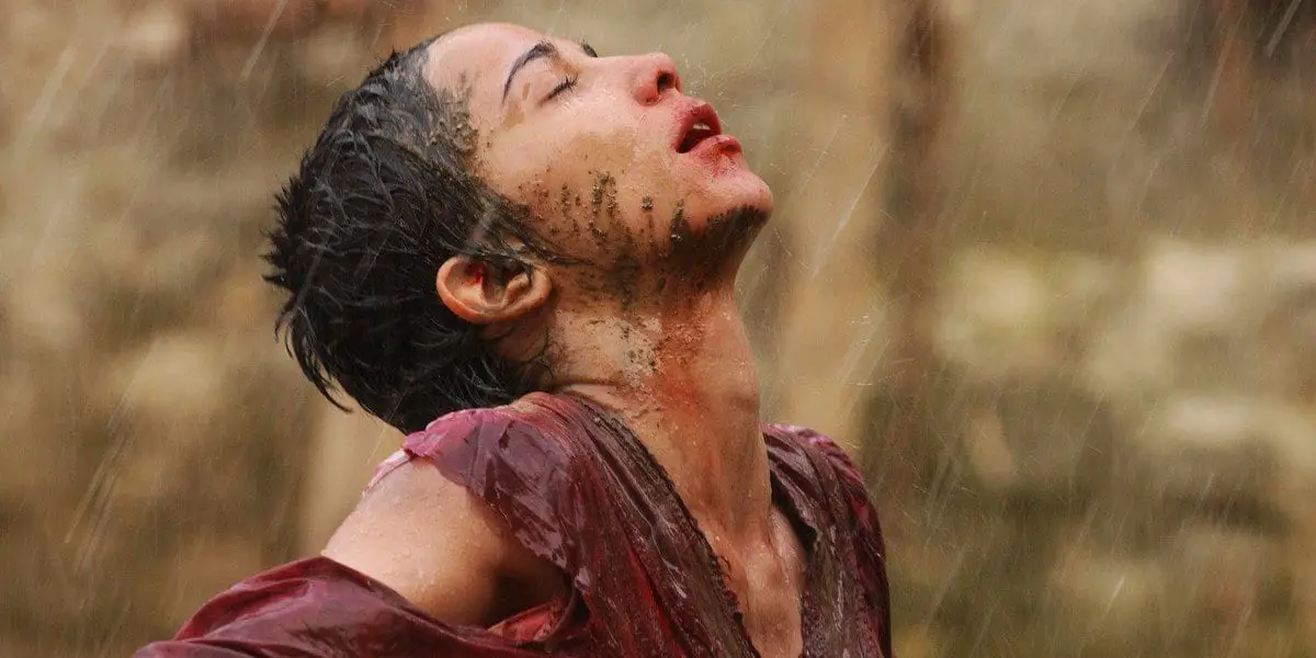 A girl, muddy and wet stands raising her face to the rain