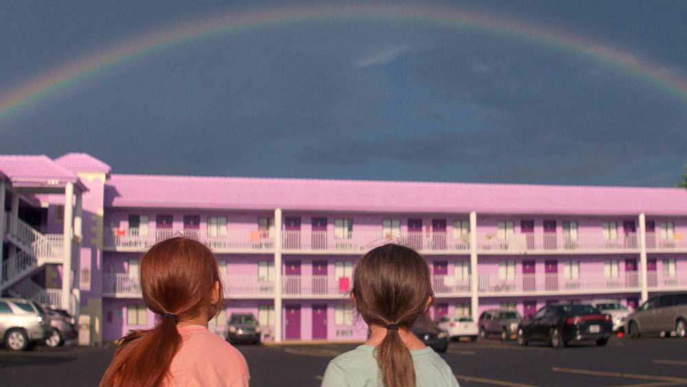2 young girls look at a rainbow above a pink motel
