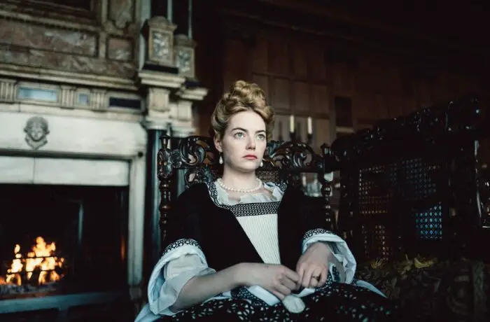 Emma Stone as Abigail in The Favourite sitting down in a classic Victorian gown.