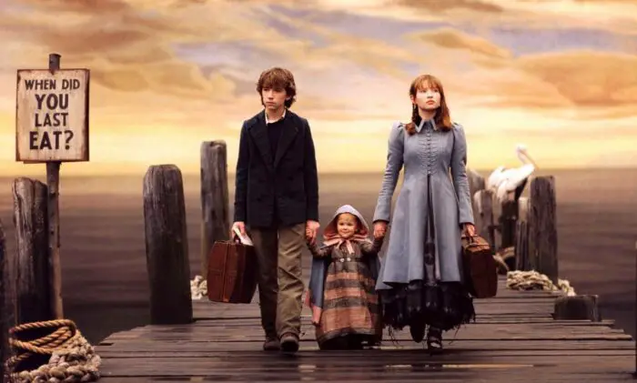 Violet Baudelaire and her brother Kraus stand on a deck with their baby sister Sunny where they wait for Lemony Snicket