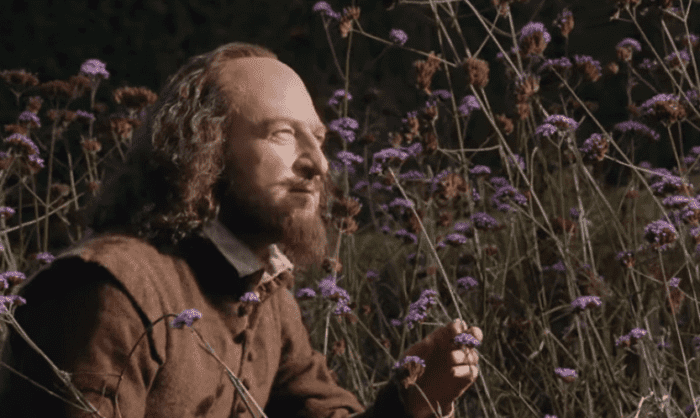 kenneth branagh as william shakespeare in tudor costume smelling flowers in a field