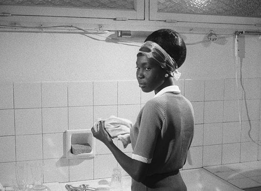 A Black woman stands at a sink washing dishes
