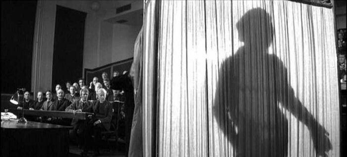 An audience looks on as the the silhouette of John Merrick looms on a curtain