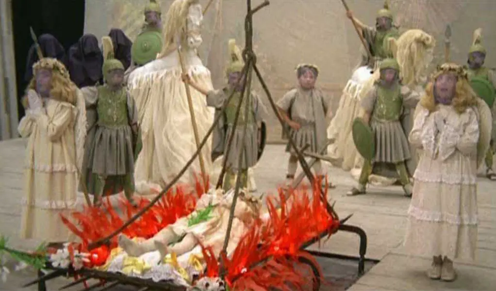 A young Giulietta is strapped to a bed of paper mache flames at her church play and surrounded by purple faced angels
