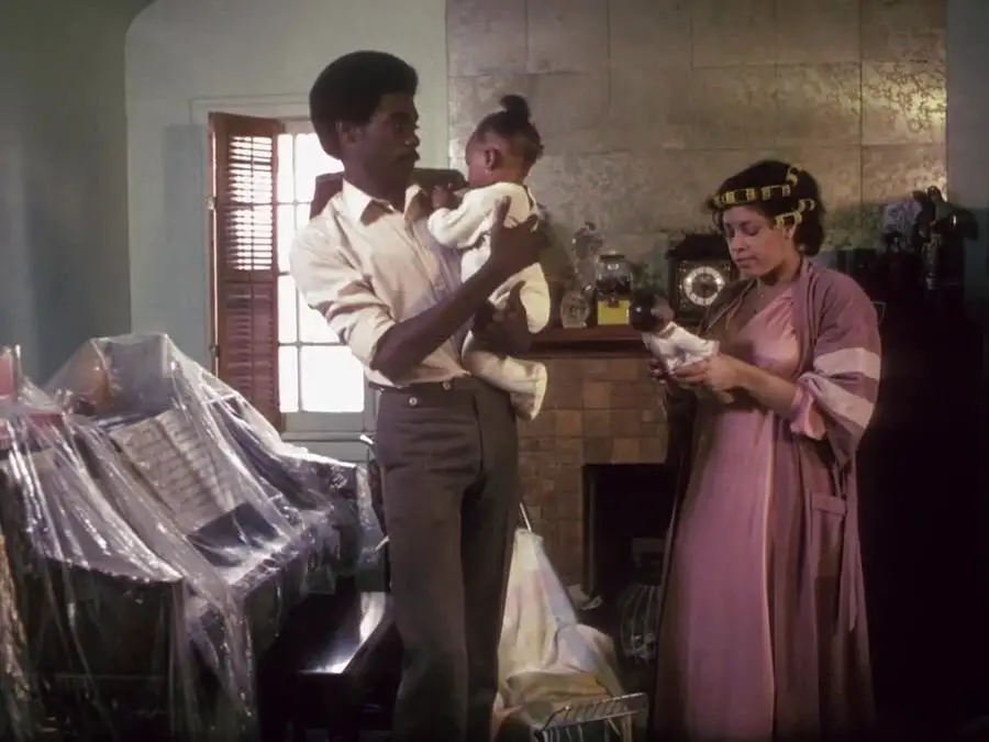 Pierce (Everett Silas) holds a baby and talks to a woman in curlers.