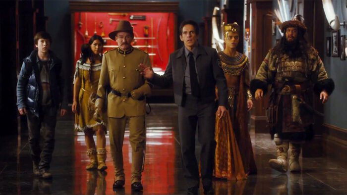 Larry Daley (Ben Stiller) stands in a museum with his right hand raised. His son, Sacajawea, Theodore Roosevelt, Ahkmenrah, and Attila the Hun are behind him.