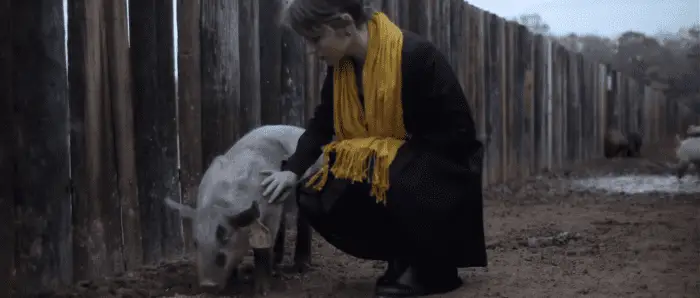 Kris (Amy Siemetz) kneels to stroke a pig in a muddy pen.