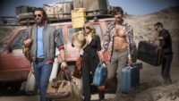 The three main characters carry their luggage from a beat up old car in an arid looking area. Credit: Netflix