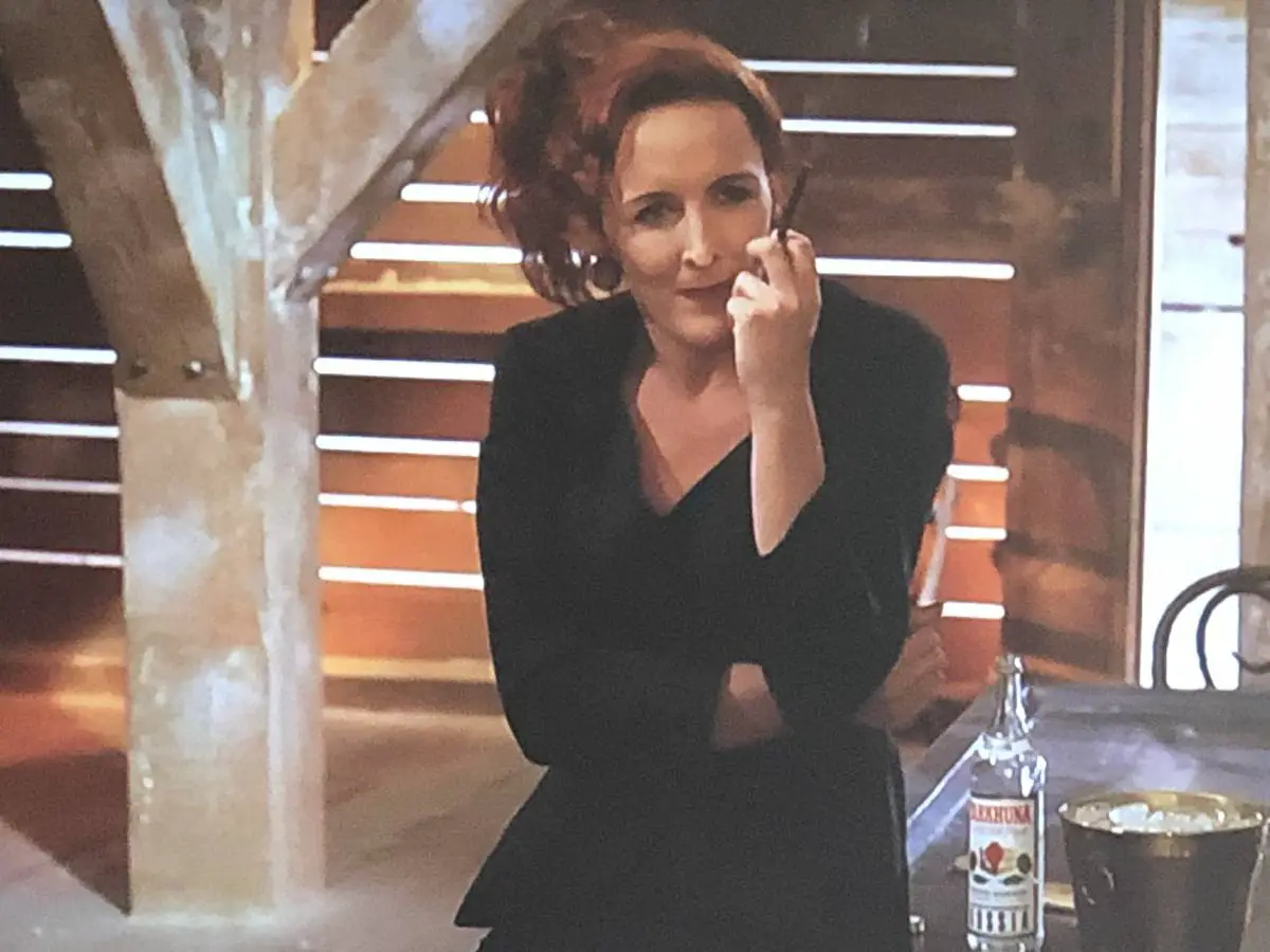 Fiona Shaw as Paulina Novacek, leaning on a desk and smoking a long cigarette