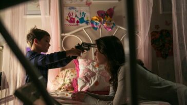 Christopher holds a gun to Emelies head as she lies on a bed