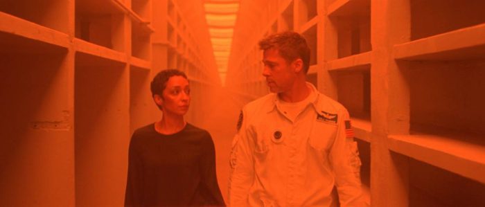 Helen Lantos and Roy McBride pass through an orange-lit hallway on subterranean Mars.