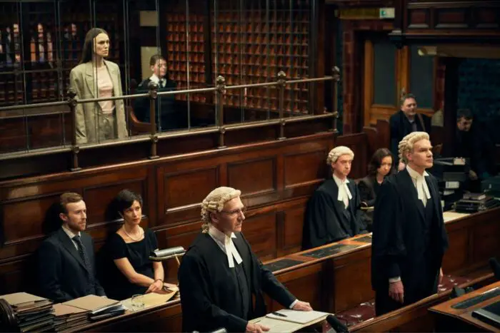 Katharine Gun (Kiera Knightley) stands in a court room awaiting the judge's verdict with her lawyer Ben Emmerson (Ralph Fiennes) and several other solicitors wearing judicial wigs