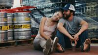 Kate (Olivia Wilde) puts her head on the shoulder of Luke (Jake Johnson) with a smile among the beer kegs of their shared workplace.