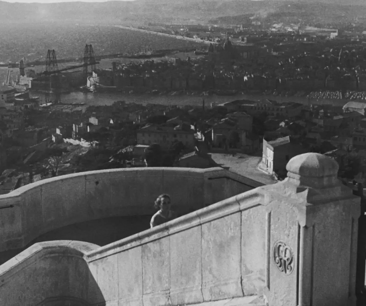 Fanny walks up church steps; in the background is a wide panorama of the port city.