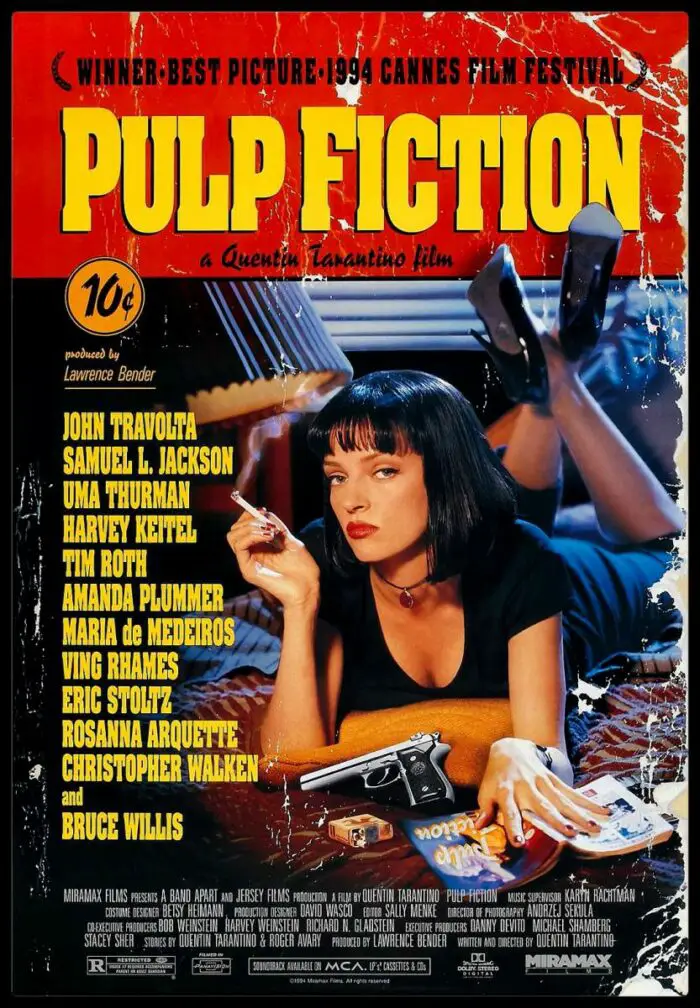 Mia Wallace lies stomach down on a motel room bed smoking a cigarette with a a gun, a pulp magazine and pack of cigarettes also on the bed