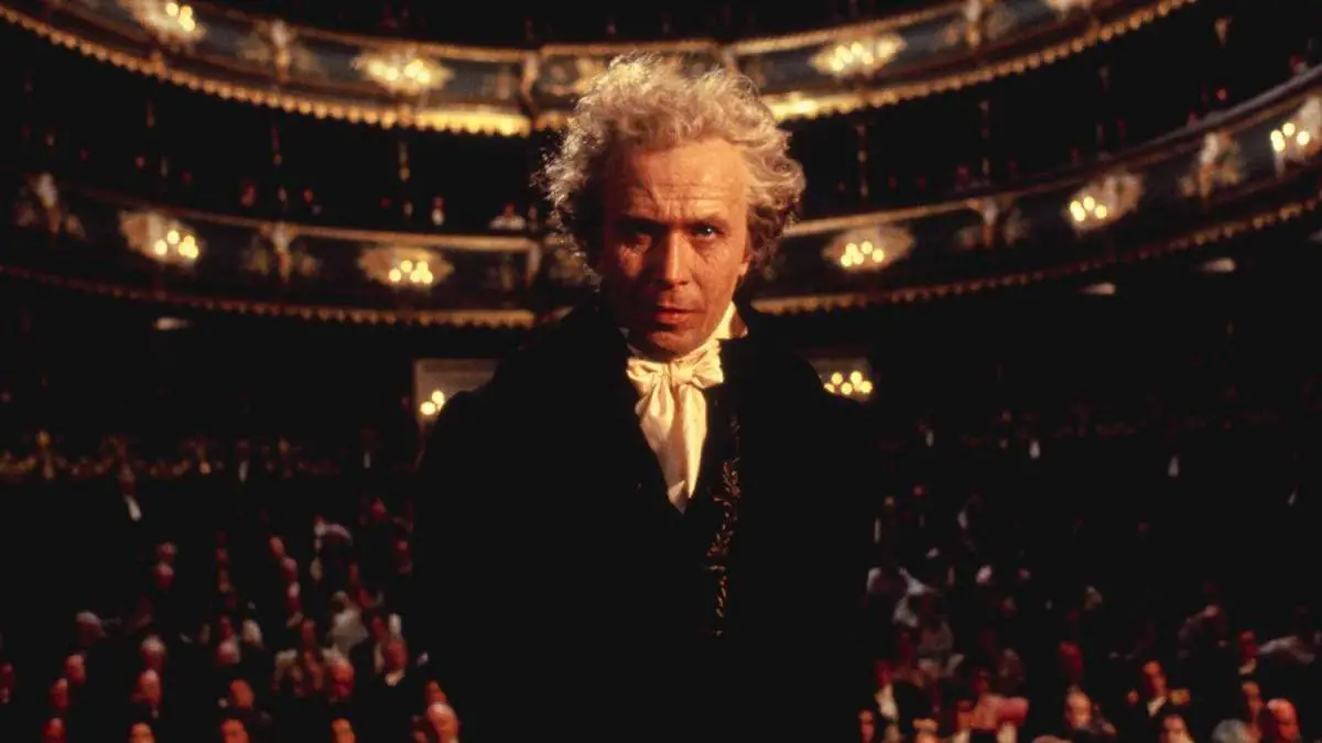 An elderly Beethoven stands on a stage, his back to the audience