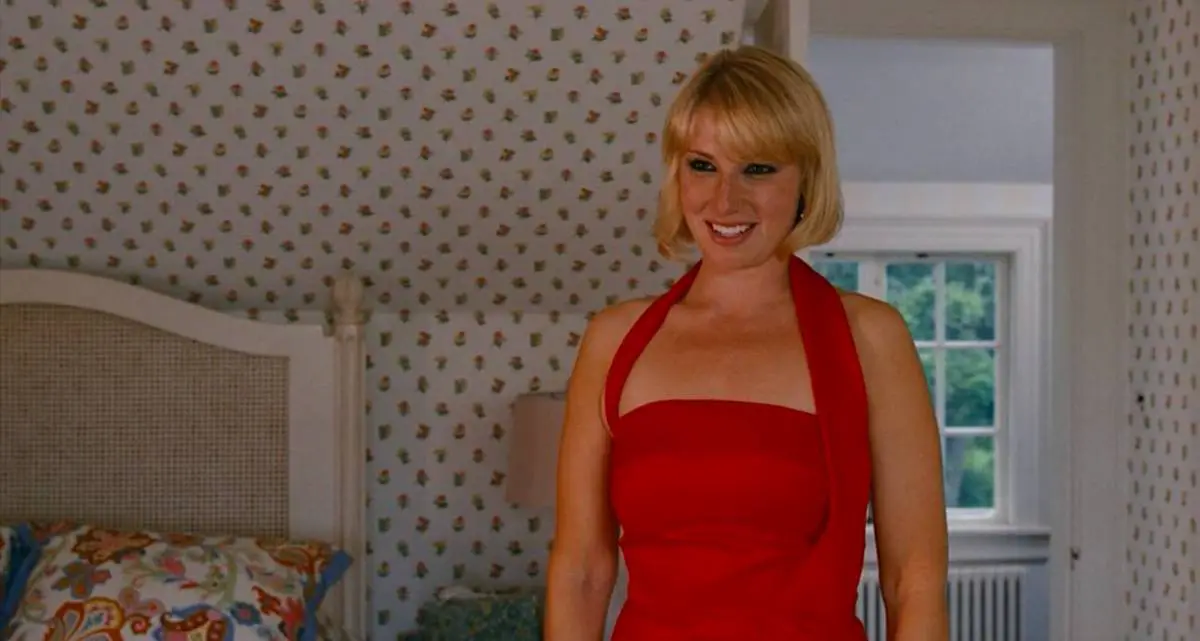 Ari Graynor as Daisy Darling, standing in her bedroom wearing a red dress for her engagement party