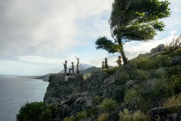 A group of children hover over a cliff's edge looking at the ocean