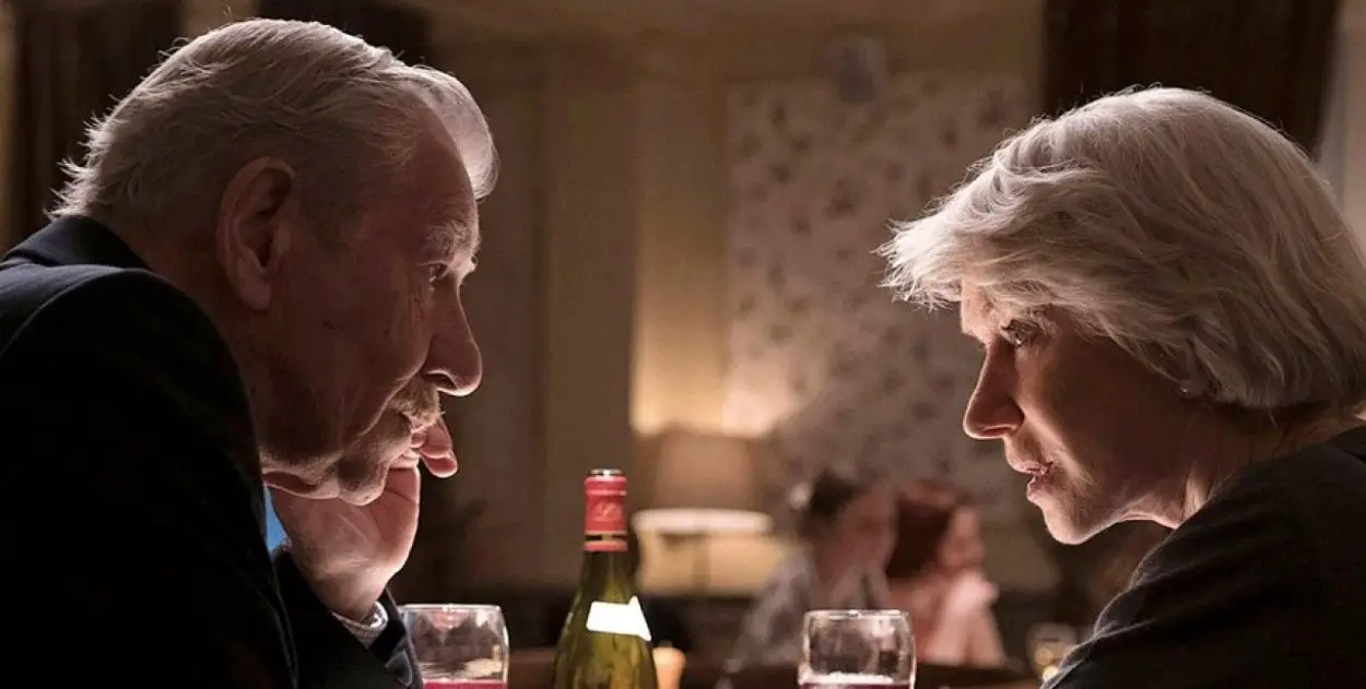 Ian McKellen and Helen Mirren speak with each other closely at a dinner table in The Good Liar