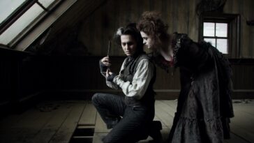 Sweeney kneels, holding a razor. Mrs Lovett leans in behind him, and he looks over his shoulder back at her