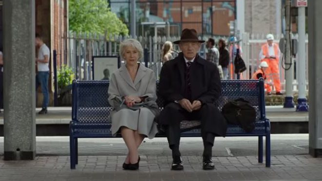 A man and a woman sit on a bench at a train station