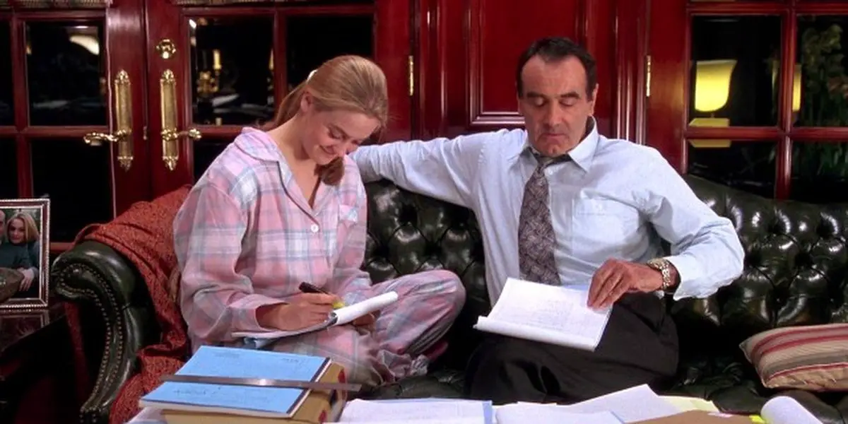 Cher and her dad sitting on a couch working on paperwork together looking down