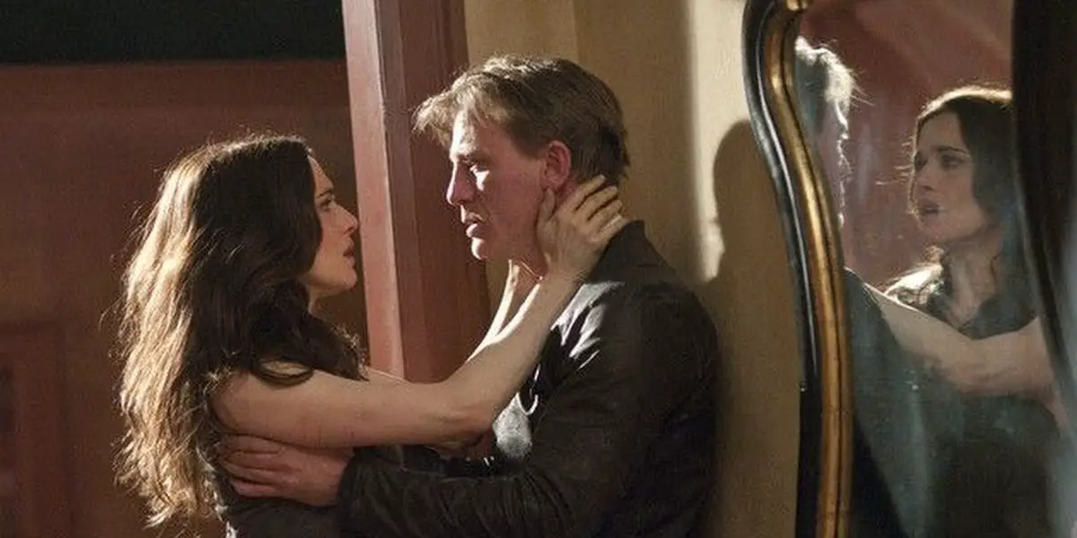 Daniel Craig and Rachel Weisz as their characters in Dream House, holding onto one another, intense expressions of pain on their faces, with their reflections in a mirror to Craig's left