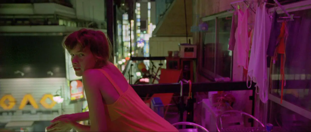 Scene early on in Enter The Void. Girl leaning over balcony with a blur of bright colours in the background