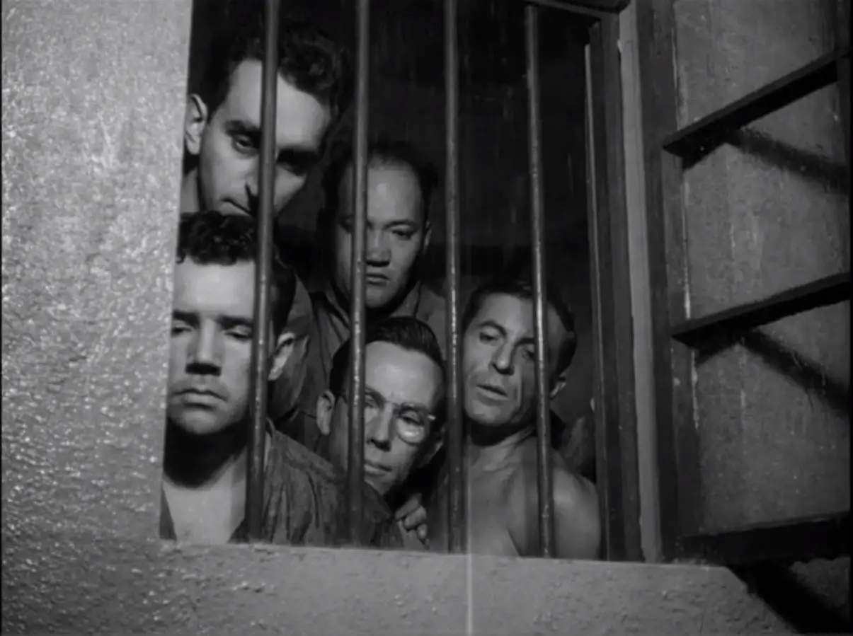 Five prisoners look out the window throw the bars of a cell 