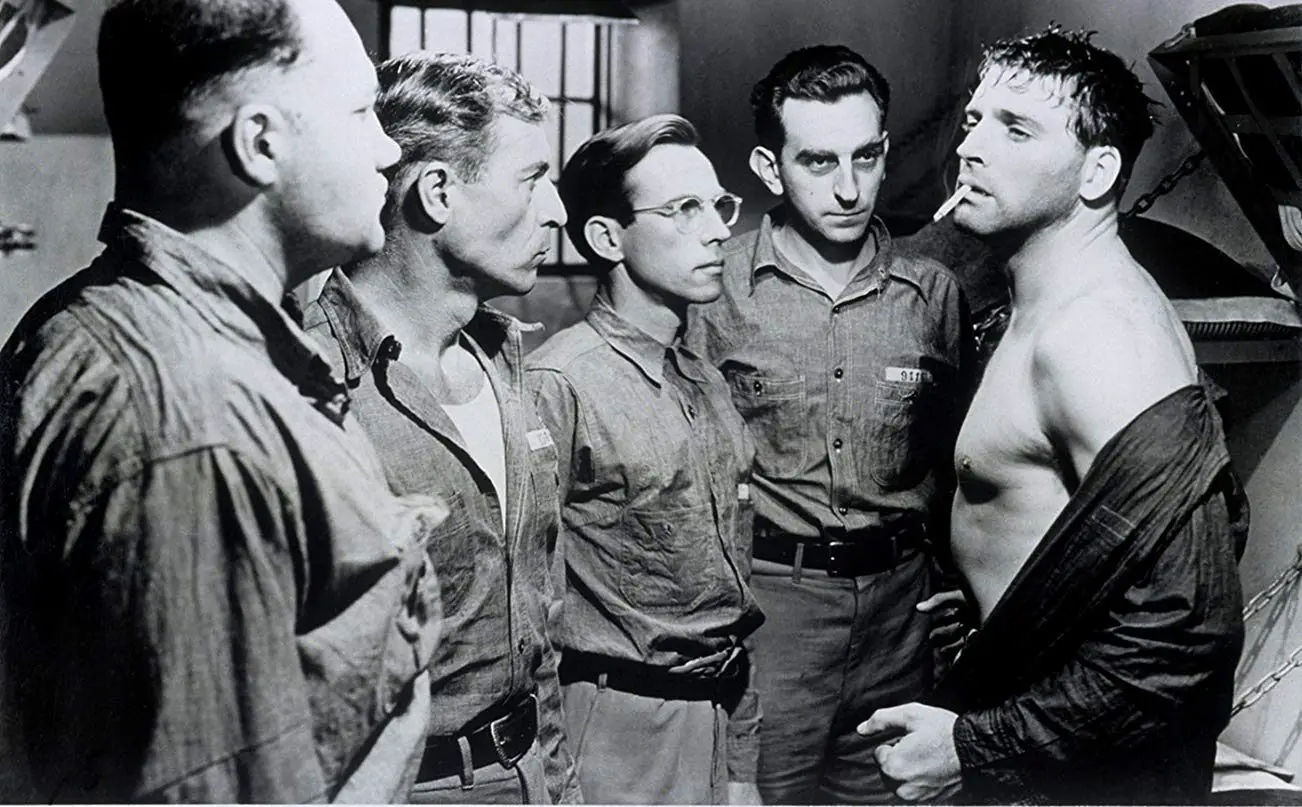 Inmates in a jail cell stare down Joe Collins (Burt Lancaster)