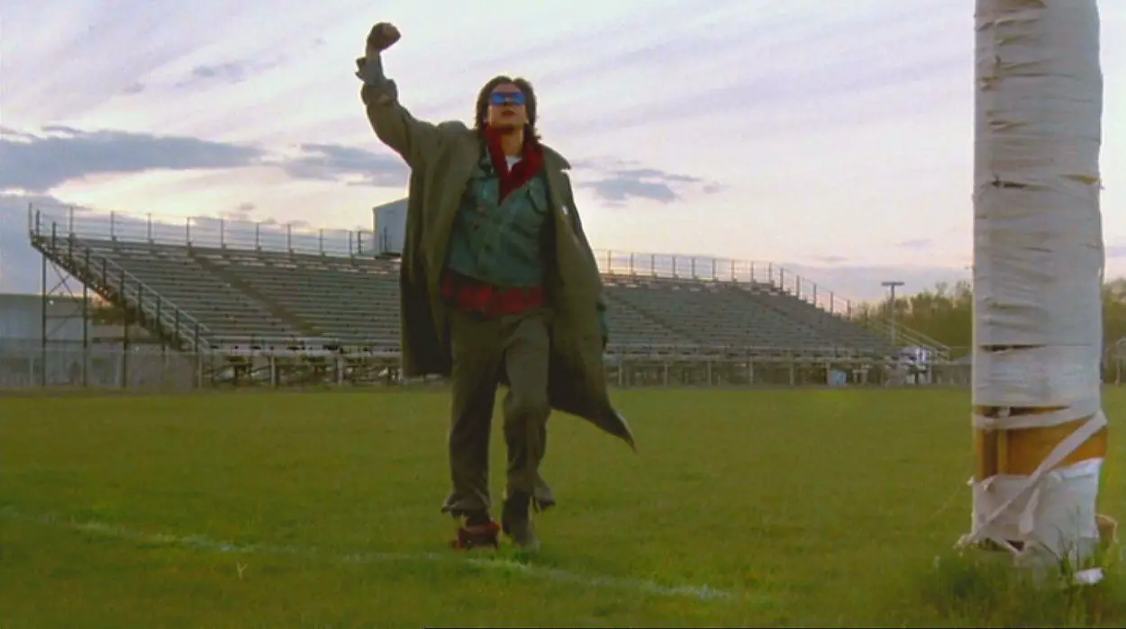 John Bender raises his fist triumphantly in the air as he walks across a school football field