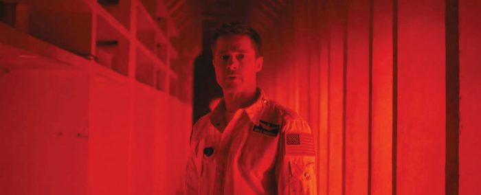 Brad Pitt stands in a red hallway looking at something unseen