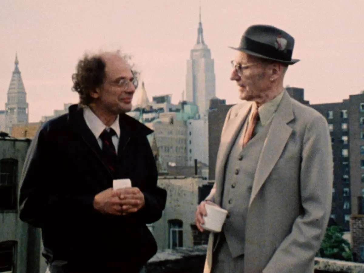 Ginsberg and Burroughs talk on a roof with the New York City Skyline behind them