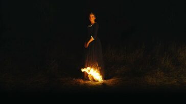 a woman stands in the dark with the tail of her dress on fire