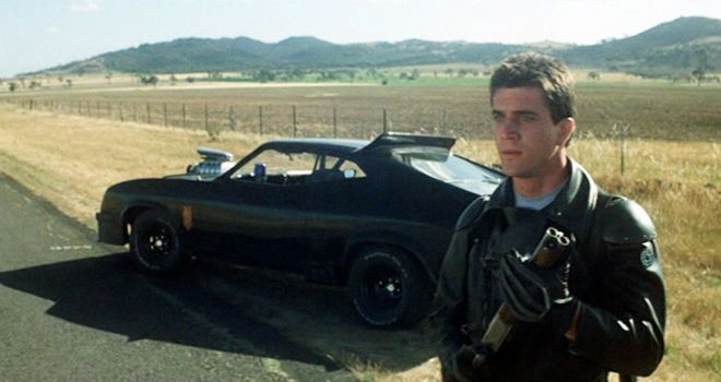 "Mad" Max Rockatansky holds his gun while standing next to his black vehicle
