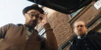 Two men with glasses look down into the trunk of a car