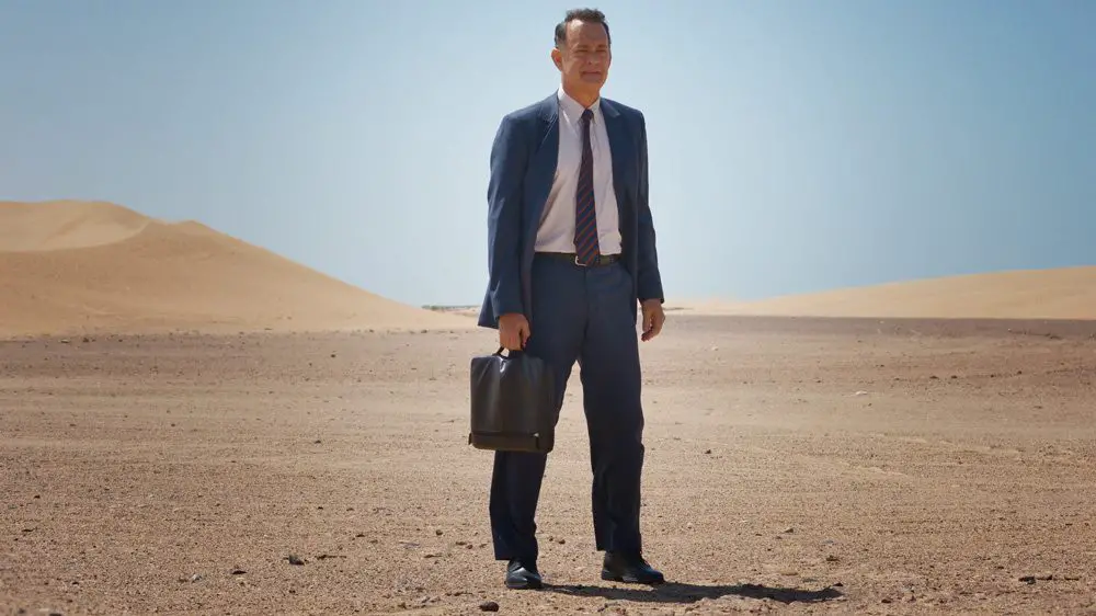 alan clay standing out in the desert in a suit and holding a briefcase