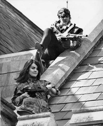 Mick and The Girl stand on the roof of the school, guns poised