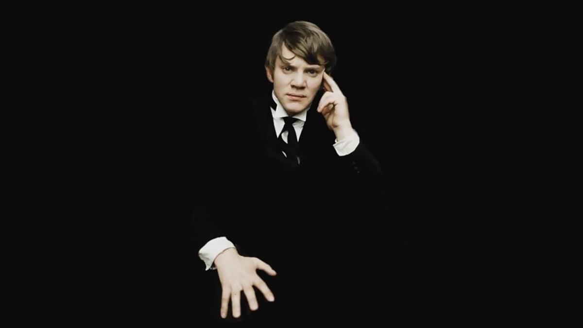 Malcolm McDowell in public school uniform poses cockily against a black background