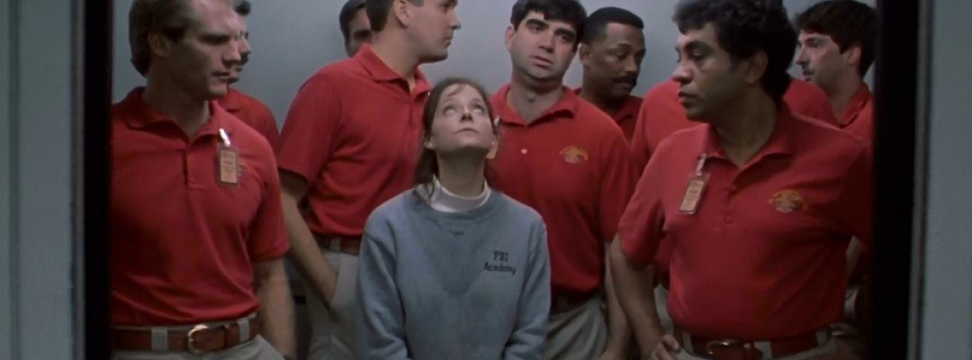 Starling stands in an elevator, surrounded by very tall male students