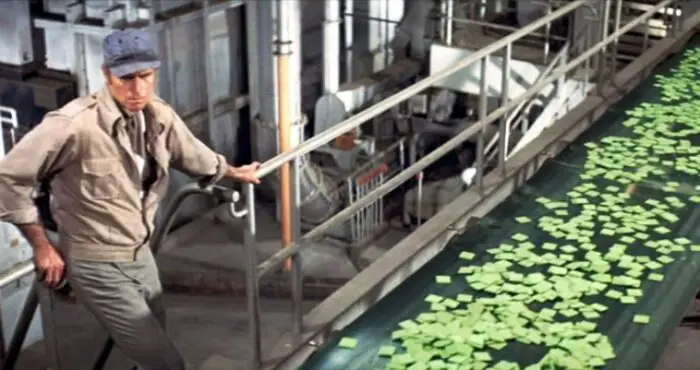 Thorn walks on the assembly line carrying Soylent Green