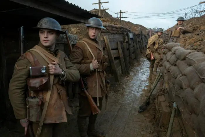 Four soldiers look at something off screen while standing in a trench