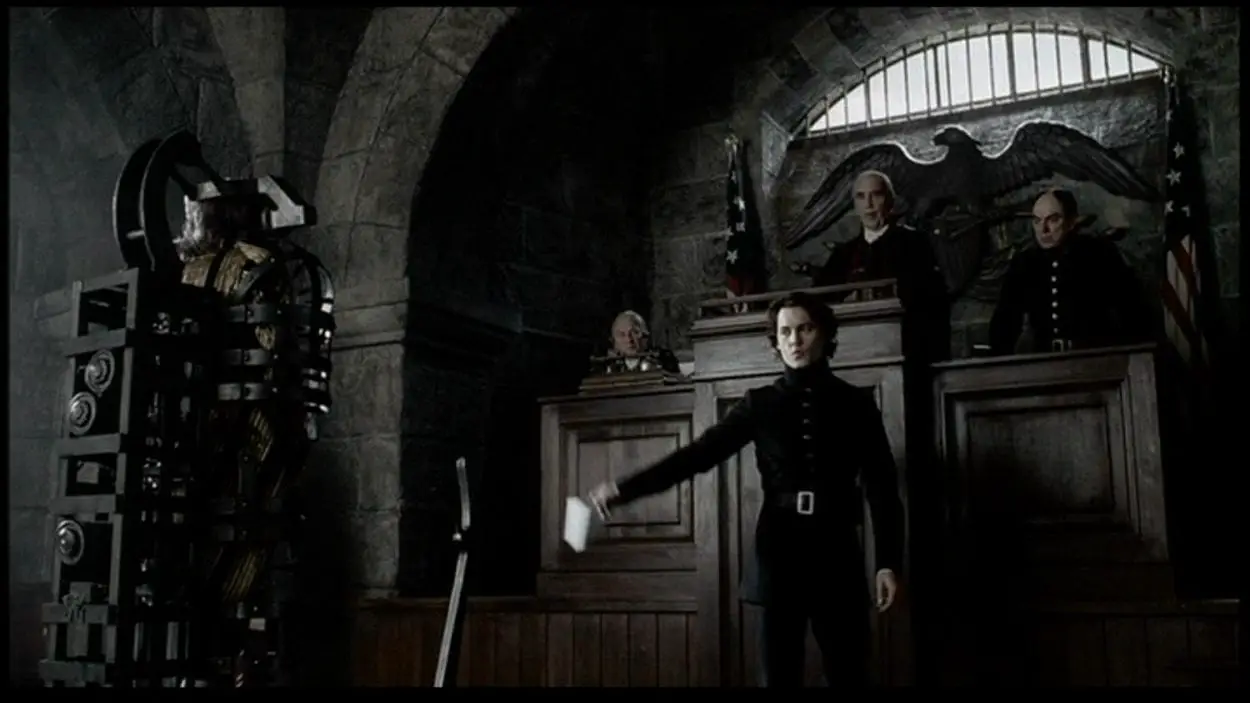 Ichabod Crane stands before a man in restraints in front of a judge in a gotic styled courtroom